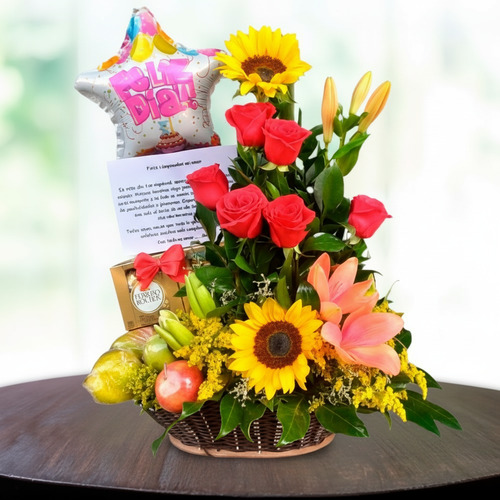 Arreglo floral de cumpleaños con globos, frutas y girasoles Canasta de mimbre con arreglo floral de rosas rojas, girasoles y lirios naranjas, acompañada de frutas, globo de cumpleaños en forma de estrella y tarjeta sobre una mesa redonda