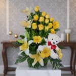 Arreglo floral exótico Amaretto con rosas amarillas, lirios blancos y gerberas, acompañado de un oso de peluche blanco con la