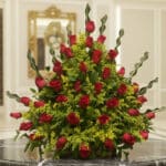 Arreglo floral premium con rosas rojas Cupido y follaje verde, sobre una mesa de mármol en un lobby de hotel boutique, ideal