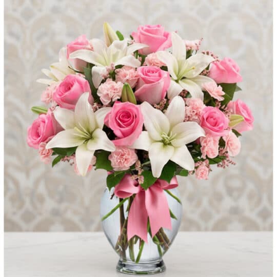 Arreglo floral vibrante con rosas rosadas, lirios blancos y claveles rosados en un jarrón de cristal con lazo rosa, ideal par
