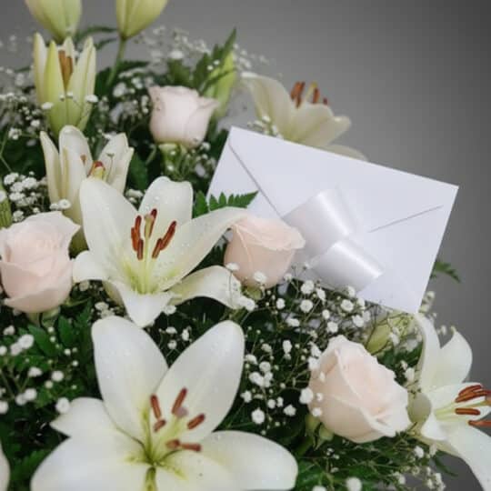 Fotografía macro premium del Arreglo Fúnebre Infinito con lirios blancos, rosas pálidas y follaje verde, con rocío sutil y ci