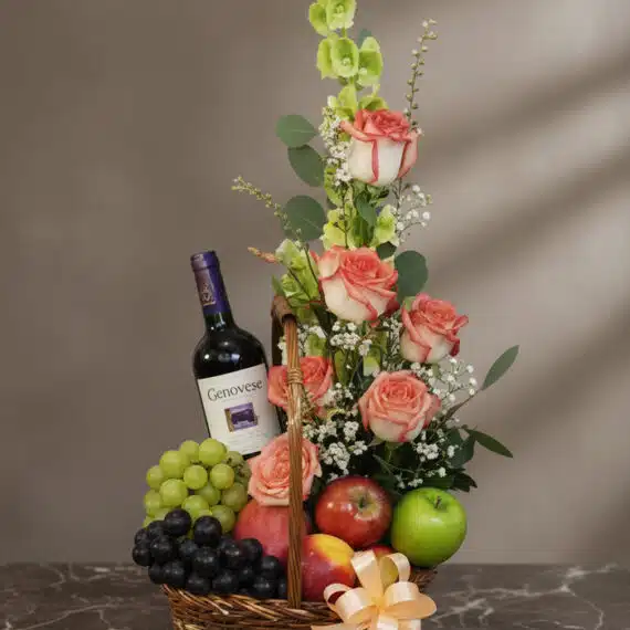 Cesta gourmet CAPRICE con rosas frescas, uvas verdes y negras, manzanas rojas y verdes, duraznos y una botella de vino tinto